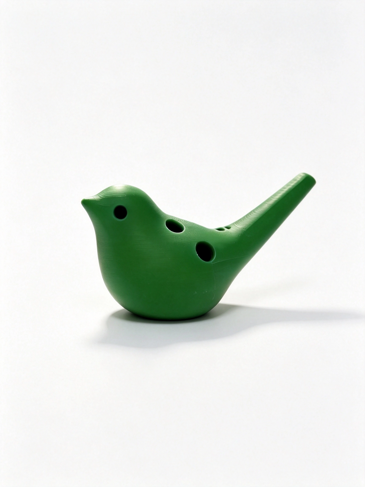 Green bird ocarina at a lower angle facing left, finger holes and the long mouthpiece in view